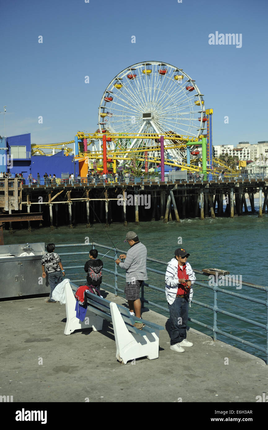 Zwei Erwachsene und zwei Kinder Angeln vom Santa Monica Pier, Pacific Park Unterhaltung fair im Hintergrund. Santa Monica, Kalifornien Stockfoto