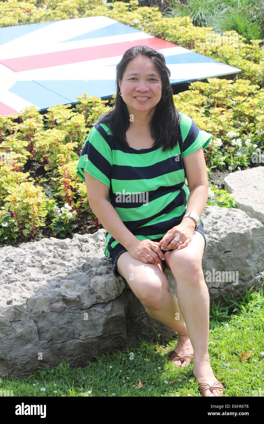 Reife, asiatische Frau sitzen auf einer niedrigen Steinmauer posiert für Fotos Stockfoto