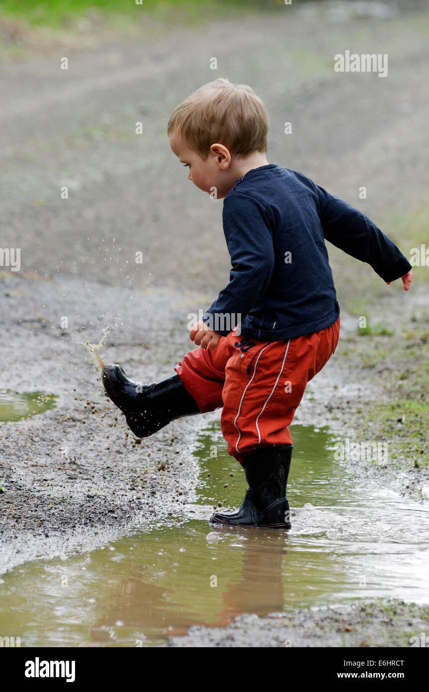 Ein kleiner Junge durchnässt läuft durch eine Pfütze Stockfoto