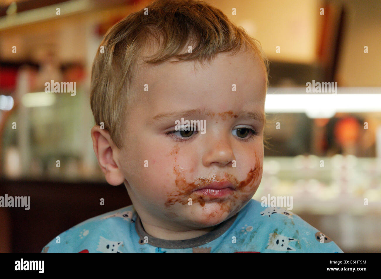 Ein zweijähriges Kind mit Schokoladensauce über das ganze Gesicht Stockfoto