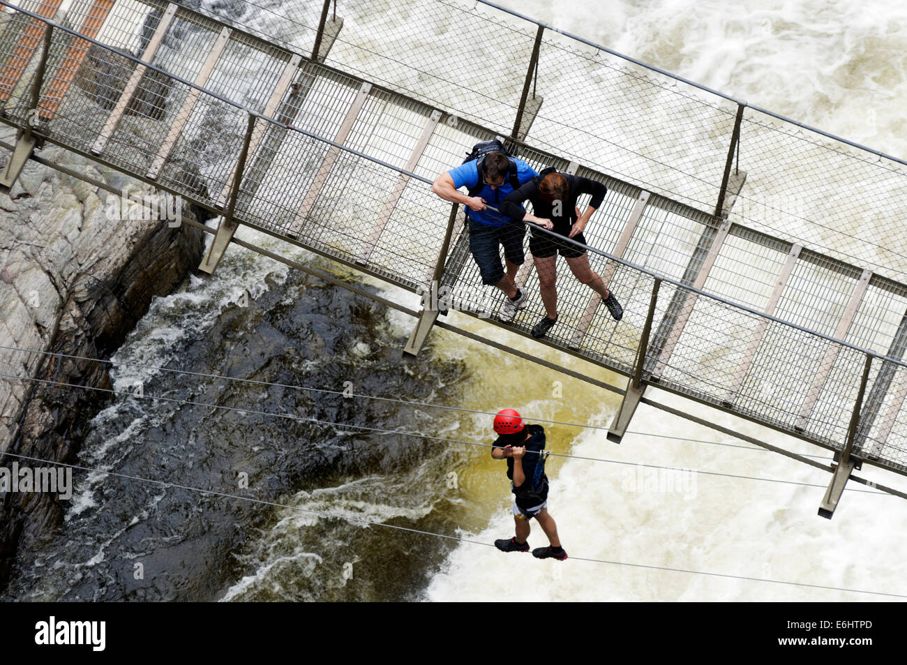 Zwei Menschen, die gerade eines Mannes Überquerung eines turbulenten Flusses auf einer Drahtbrücke in Canyon Ste Anne in Quebec, Kanada Stockfoto