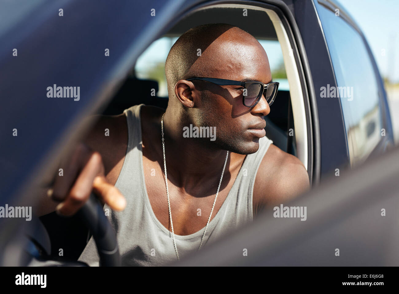 Afrikanische Männermodel in seinem Auto. Stilvolle junger Mann mit Händen am Lenkrad. Muskulösen jungen Sonnenbrille wegsehen. Stockfoto