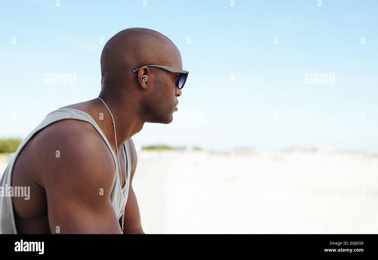 Schuss von einem jungen Mann mit Sonnenbrille im Freien. Afrikanischen jungen Mann sitzt am Strand bei textfreiraum wegsehen. Stockfoto
