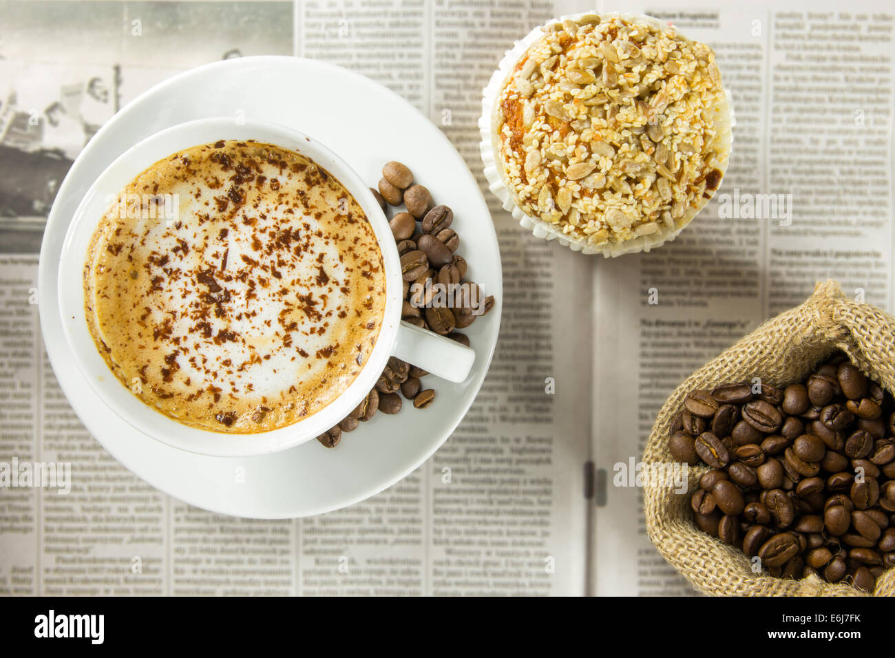 Tasse Kaffee, gerösteten Bohnen und einen Muffin, angeordnet auf einer Zeitung Stockfoto