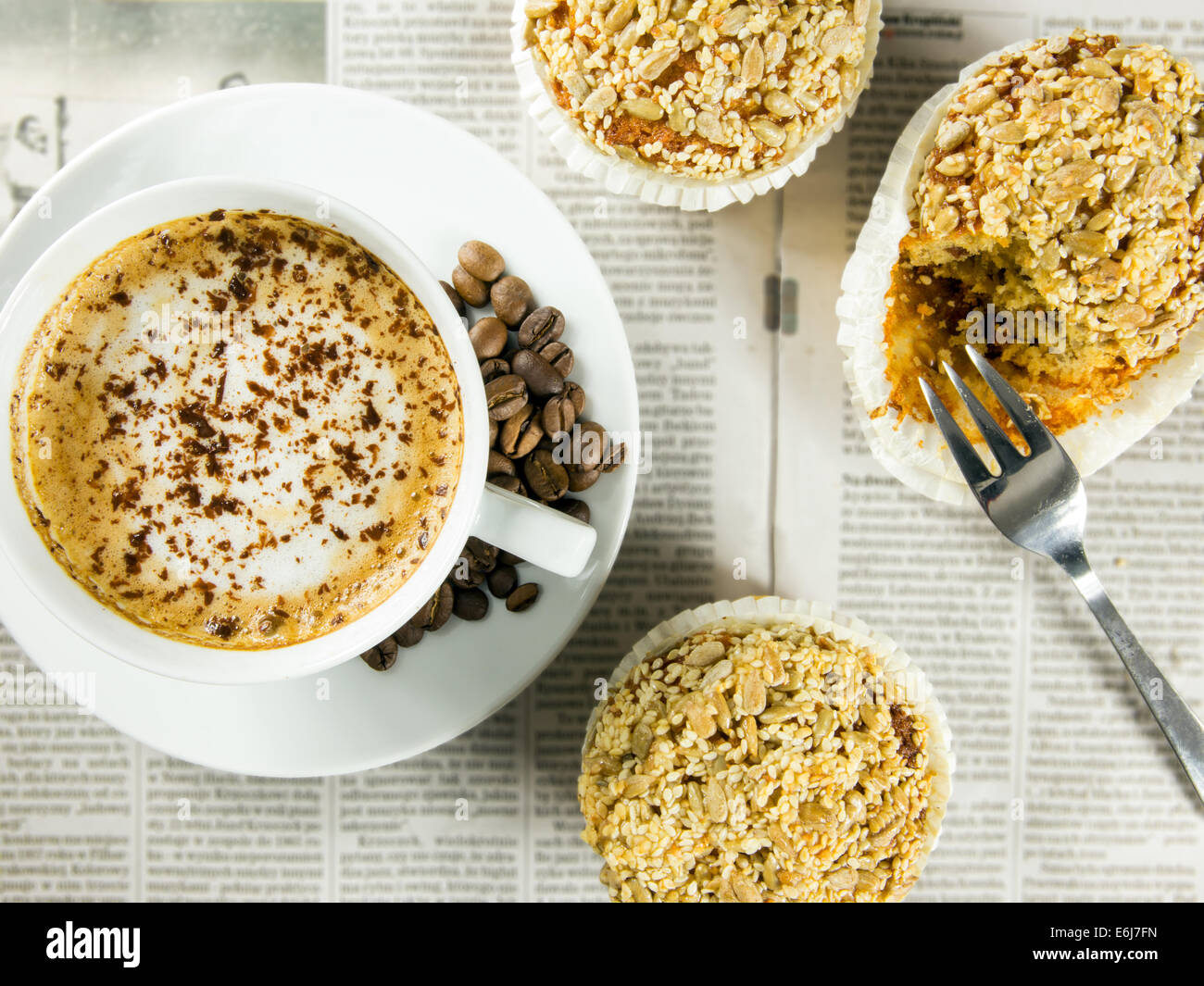 Tasse Kaffee, gerösteten Bohnen und Muffins, angeordnet auf einer Zeitung Stockfoto