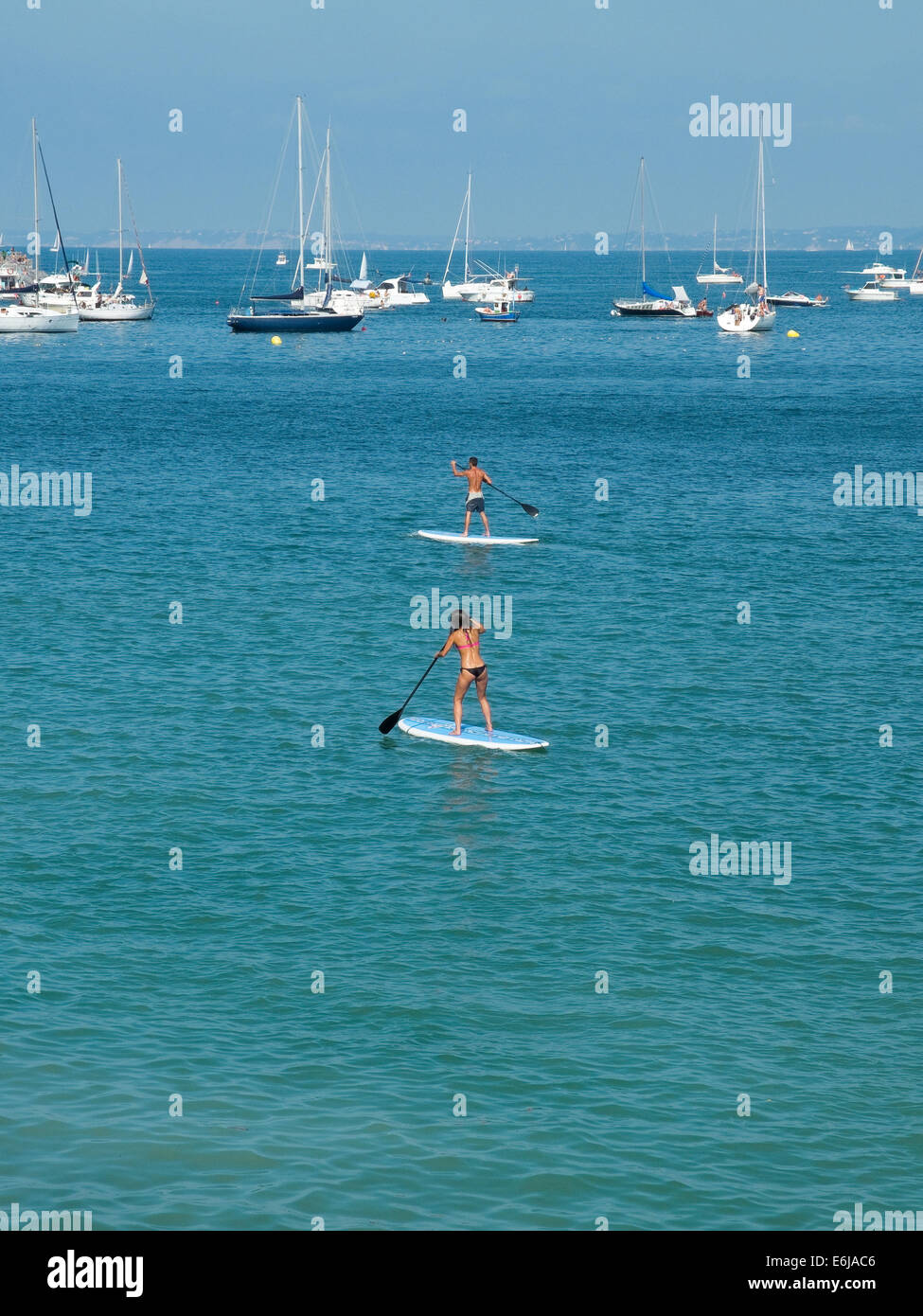 SUP, Paddle Surf am Strand mit Booten im Hintergrund. Stockfoto