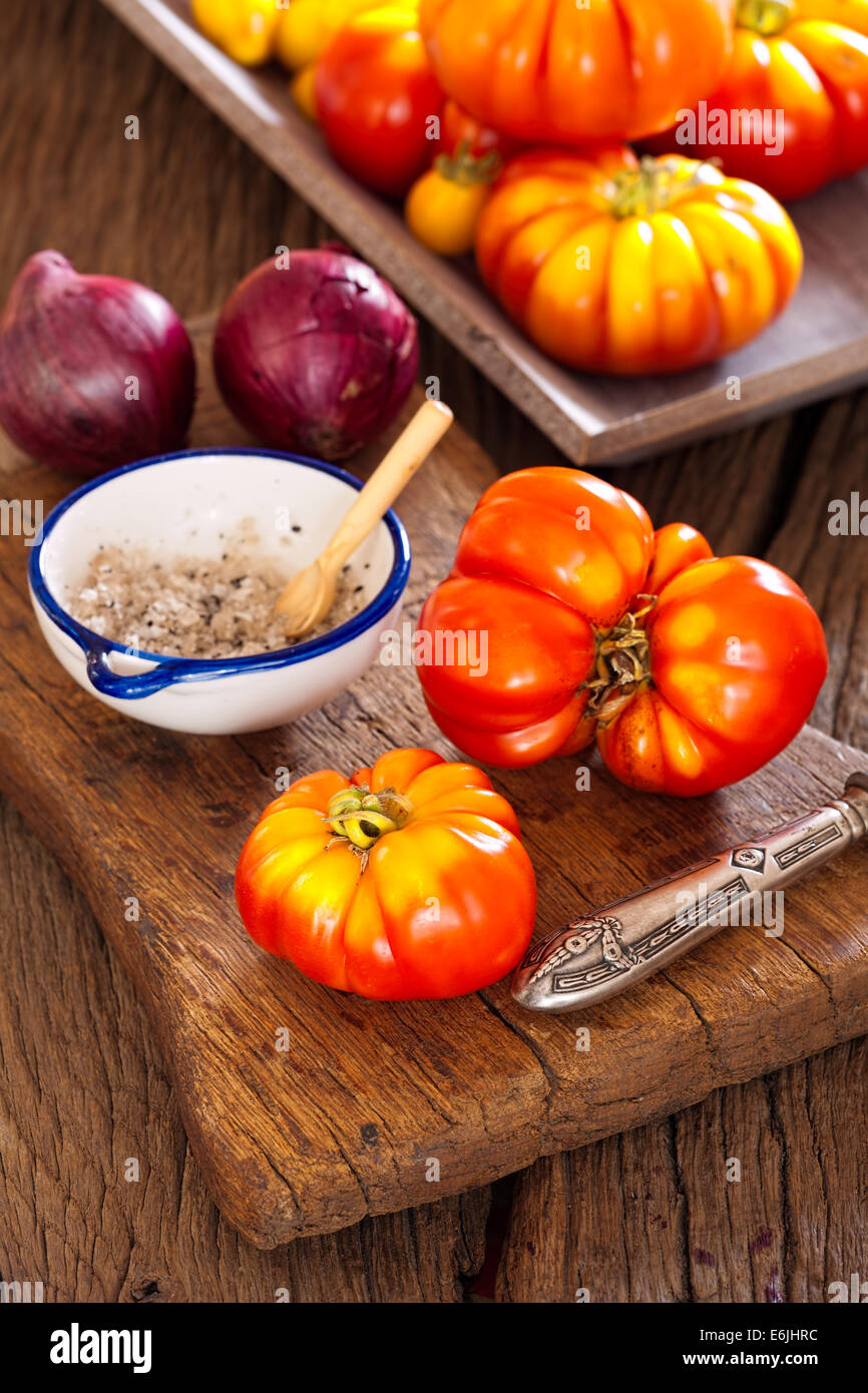 Frisches Rindfleisch Tomaten aus dem eigenen Garten mit einem Messer, Zwiebeln und Salz auf ein altes rustikales Schneidebrett im Landhausstil Stockfoto