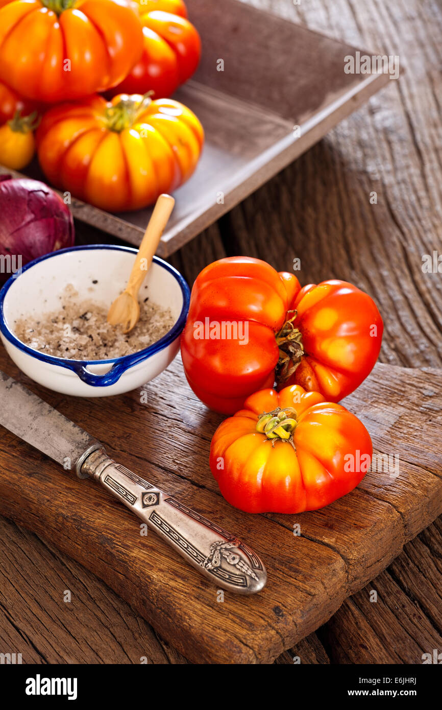 Fleischtomaten, Salz Schüssel und Löffel mit einem Messer Zwiebeln auf ein altes rustikales Schneidebrett im Landhausstil Stockfoto