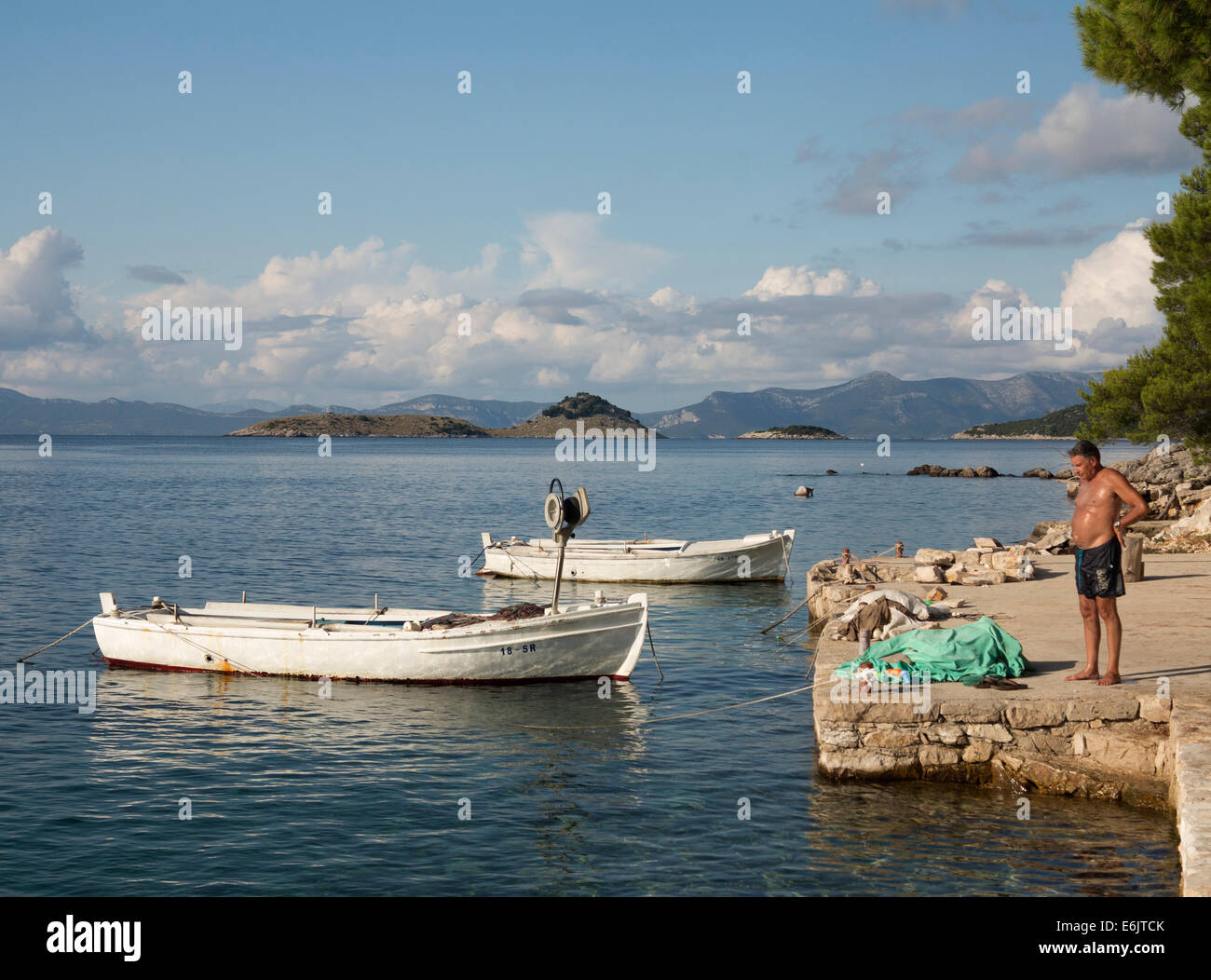 Mann im Schwimmen shorts stehen am Hafen auf der Insel Mljet in Kroatien mit weißen Angelboote/Fischerboote vor Anker in der Nähe Stockfoto
