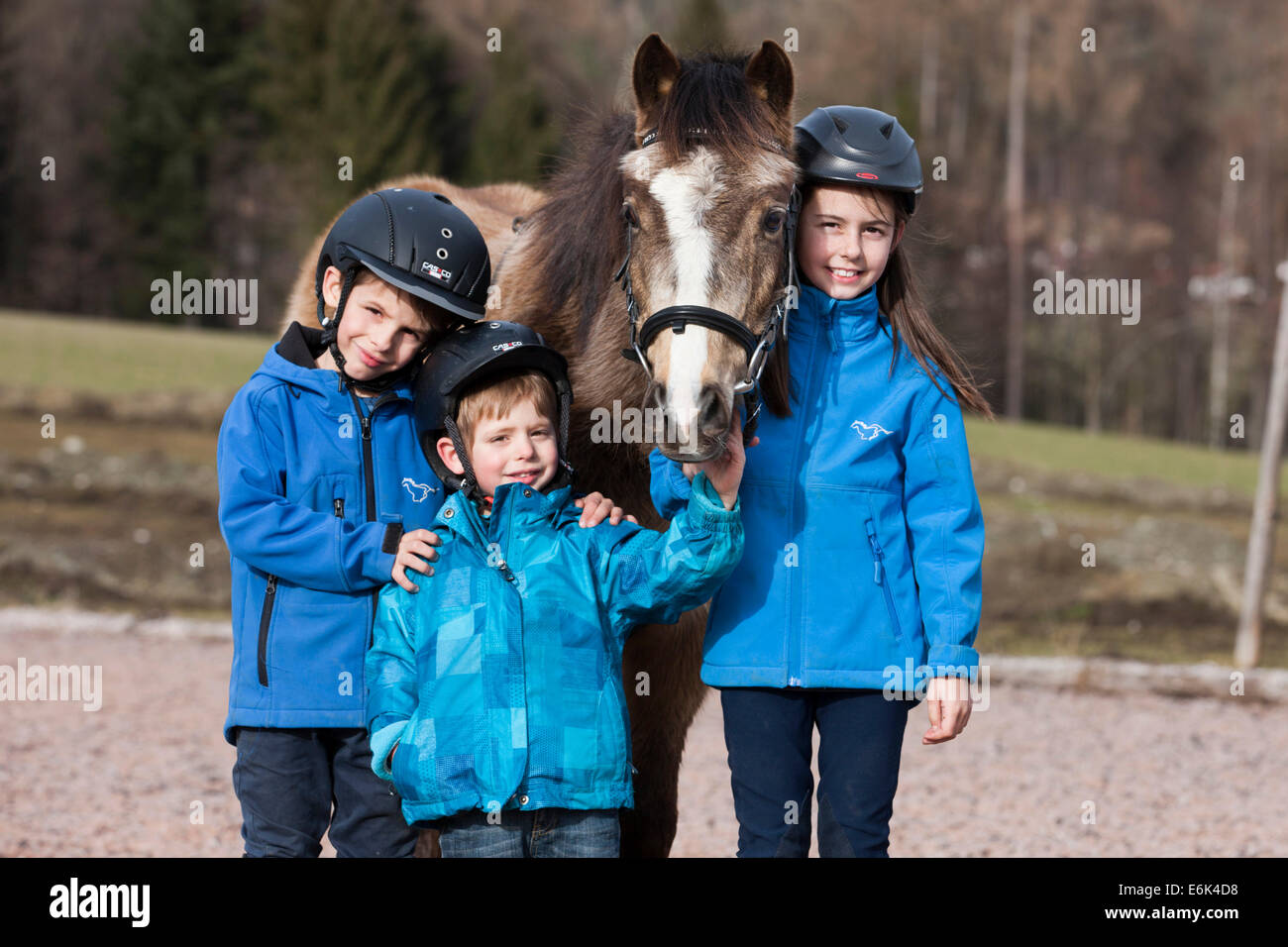 Drei Kinder tragen dun Reithelme stehen neben einem Pony, mit einen Zaum, Tirol, Österreich Stockfoto