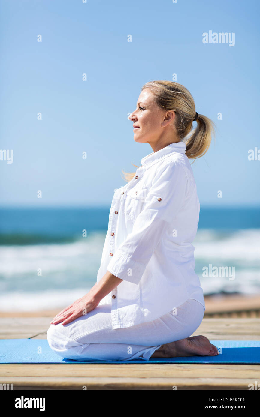 schöne mittlere gealterte Frau tun Yoga am Strand Stockfoto