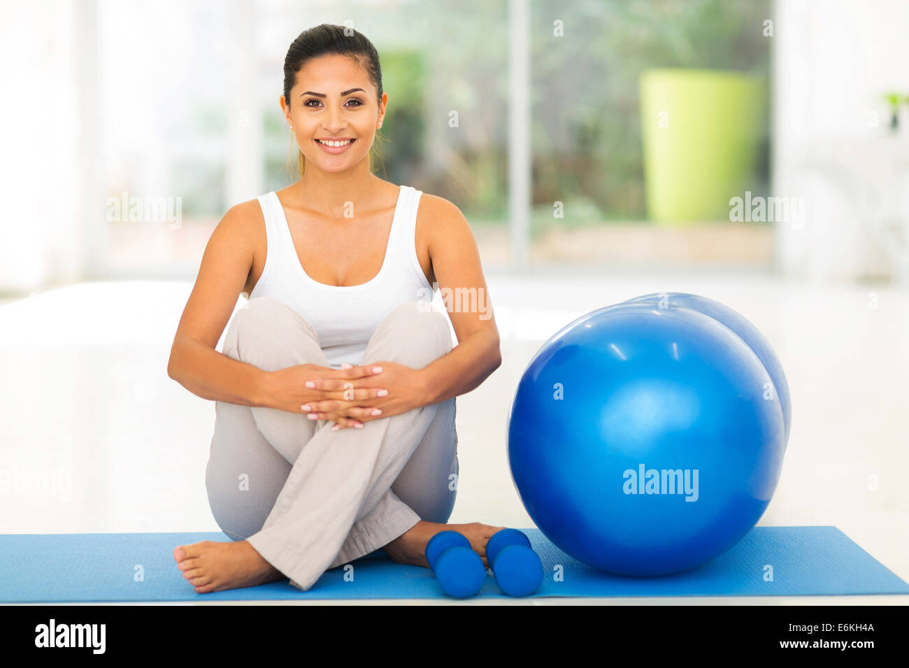 wunderschöne junge Frau sitzt auf der Matte mit Gymnastikball Stockfoto