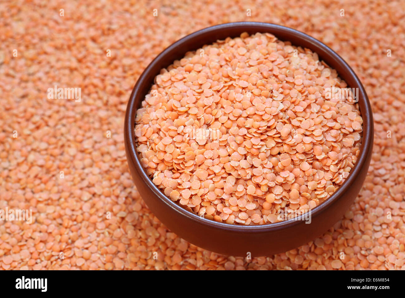 Rote Linsen in einer Schüssel auf einem Hintergrund von roten Linsen. Closeup. Stockfoto