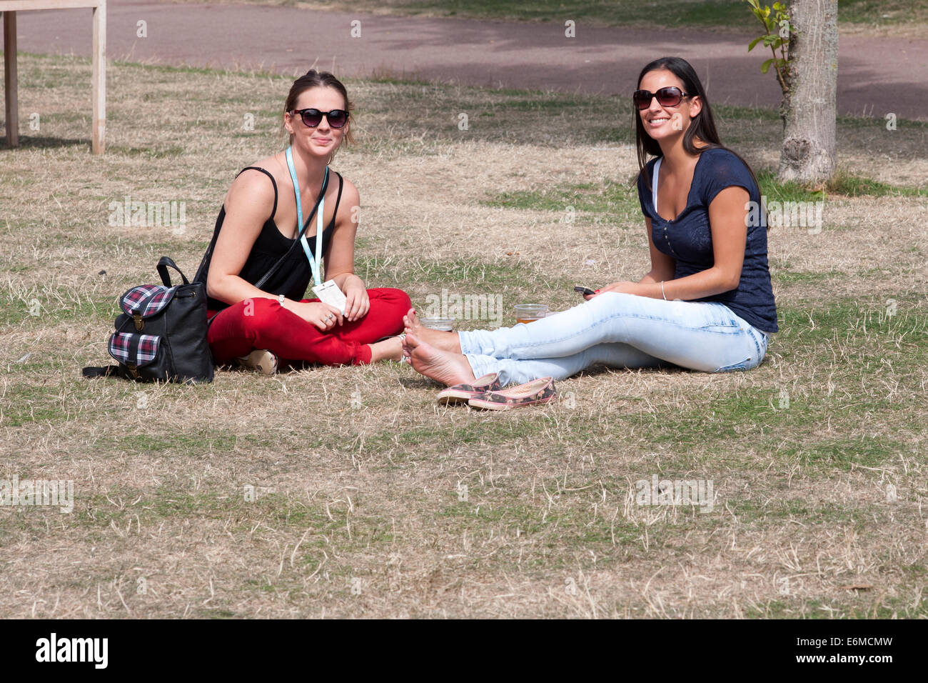 zwei hübsche junge Frauen saßen auf dem Rasen genießen die Atmosphäre bei der siegreichen Festival 2014 Southsea England uk Stockfoto