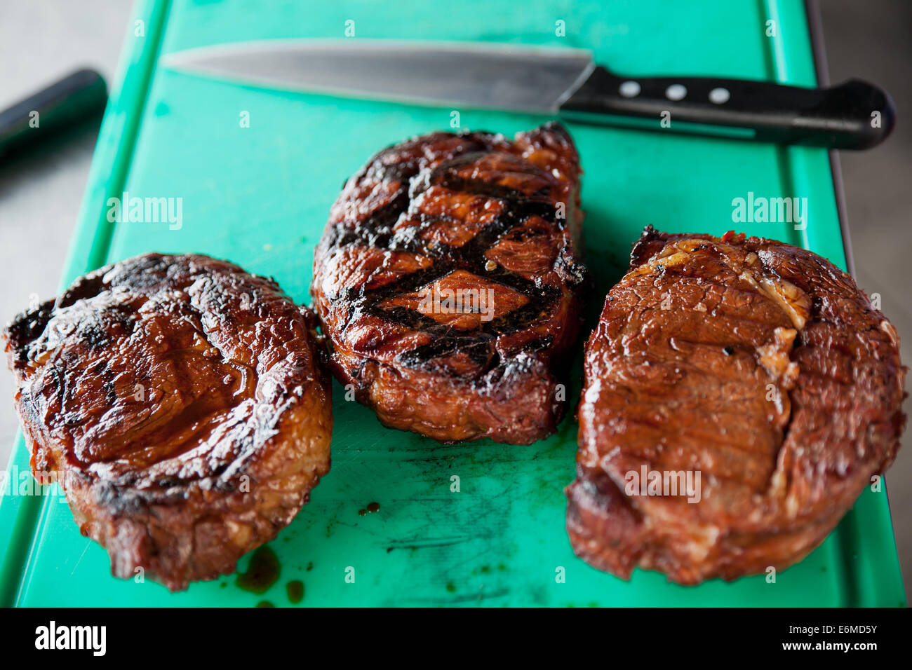 Schöne Trilogie von gegrillte Rib-Eye-Steaks auf einem grünen Schneidebrett mit einem großen Messer. Stockfoto