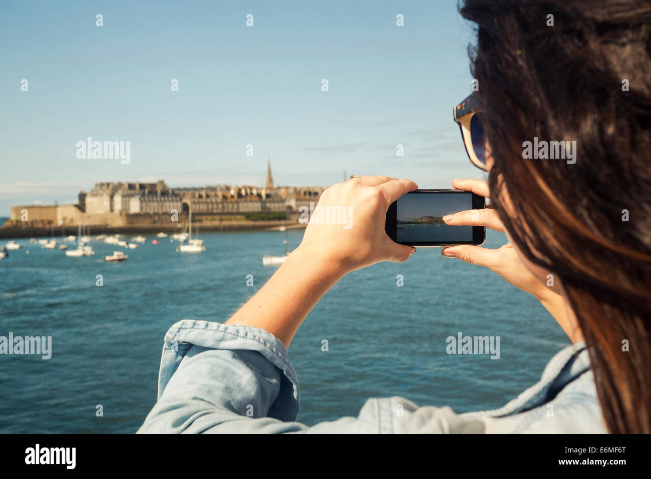 Junge Frau fotografiert die historische ummauerte Stadt St. Malo, Frankreich, von einem Boot aus auf einem sonnigen Urlaub. Stockfoto