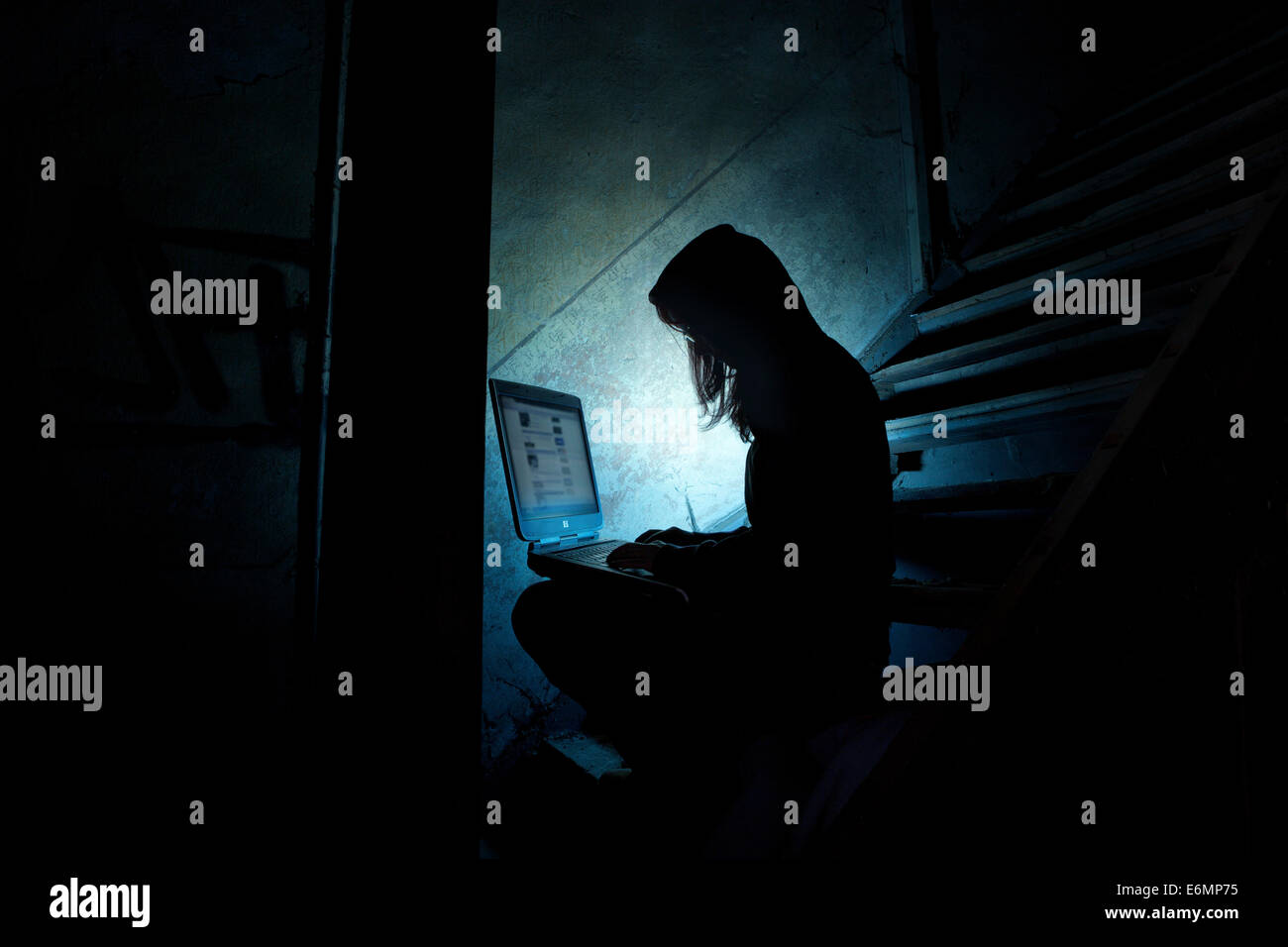 Weibliche Computerhacker sitzen mit einem Laptop in der Dunkelheit, in einem alten Gebäude Stockfoto