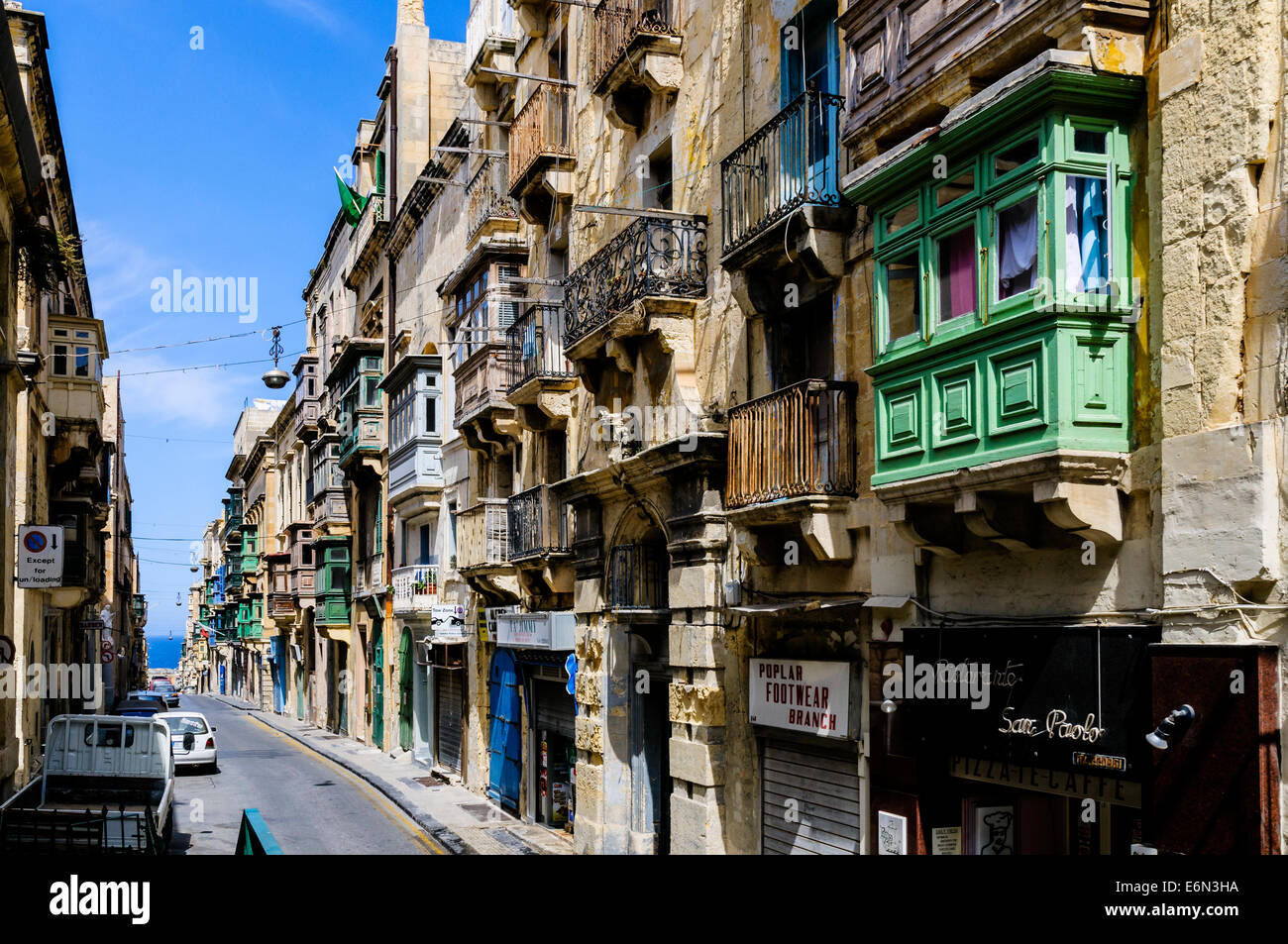 Eine typische Valletta Straße von alten mittelalterlichen Paläste mit Holz- und reich verzierten gusseisernen Balkonen über moderne Ladenfronten fronted Stockfoto