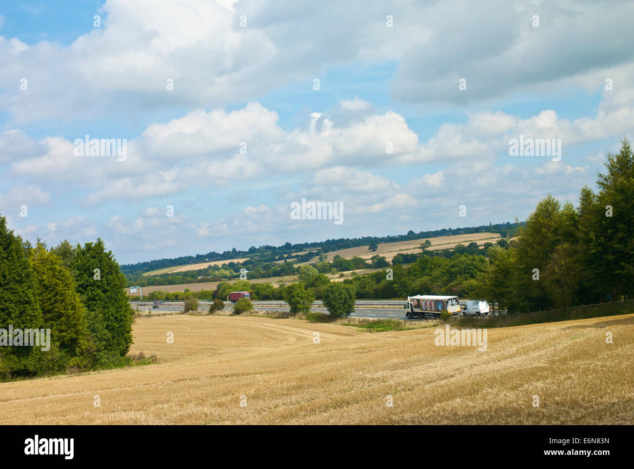 Verkehr auf M40 Autobahn vorbei an Feldern vor kurzem Schnitt Pflanzen und strahlend blauem Himmel Hintergrund. Stockfoto