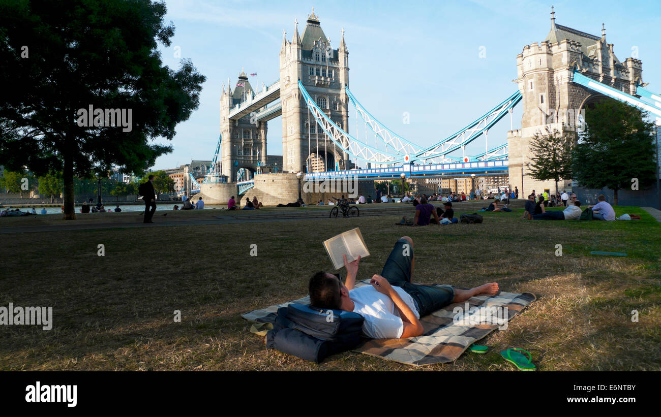 Ein Mann, der an einem Sommerabend im Park an der Themse auf einer Decke liegt und einen Blick auf die Tower Bridge Central London England UK KATHY DEWITT hat Stockfoto