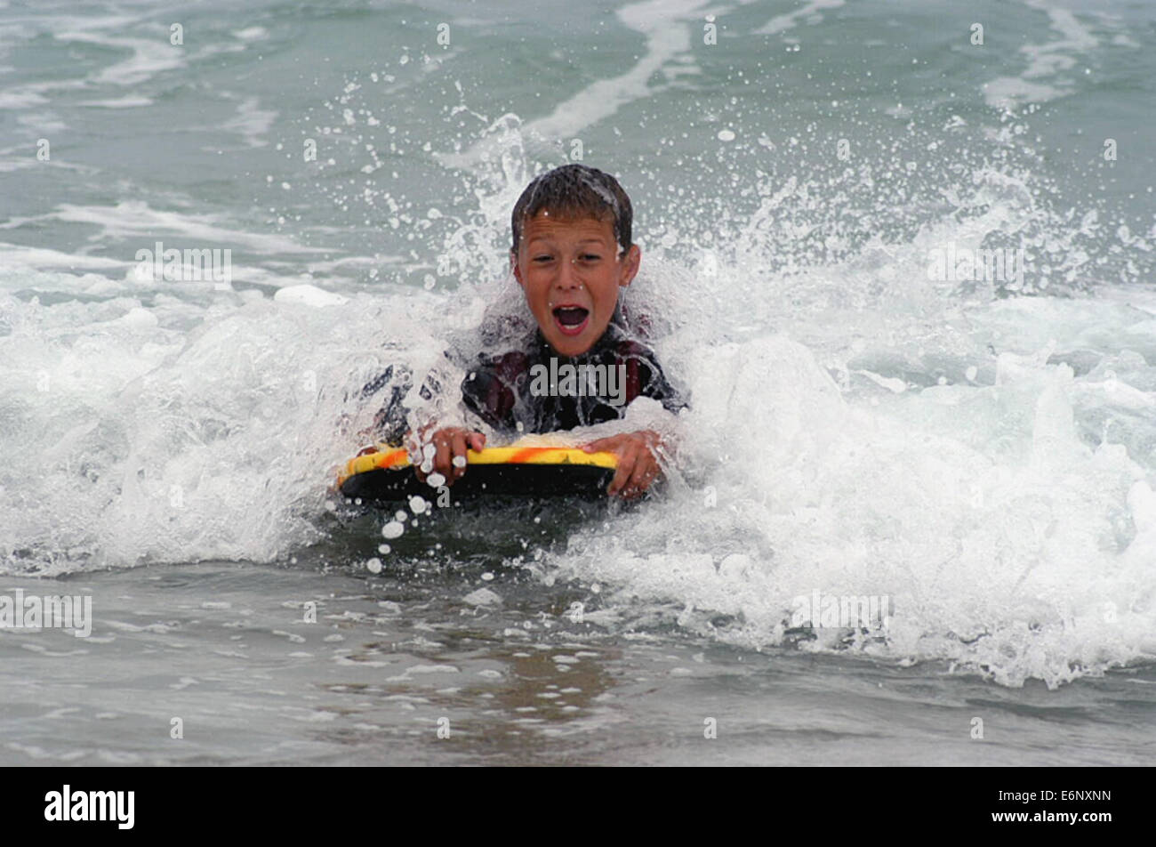 Junge männliche Jugendliche Surfen auf einem Bodyboard im Meer mit einer Welle um und über ihn zu brechen, lachen, einen Neoprenanzug tragen Stockfoto