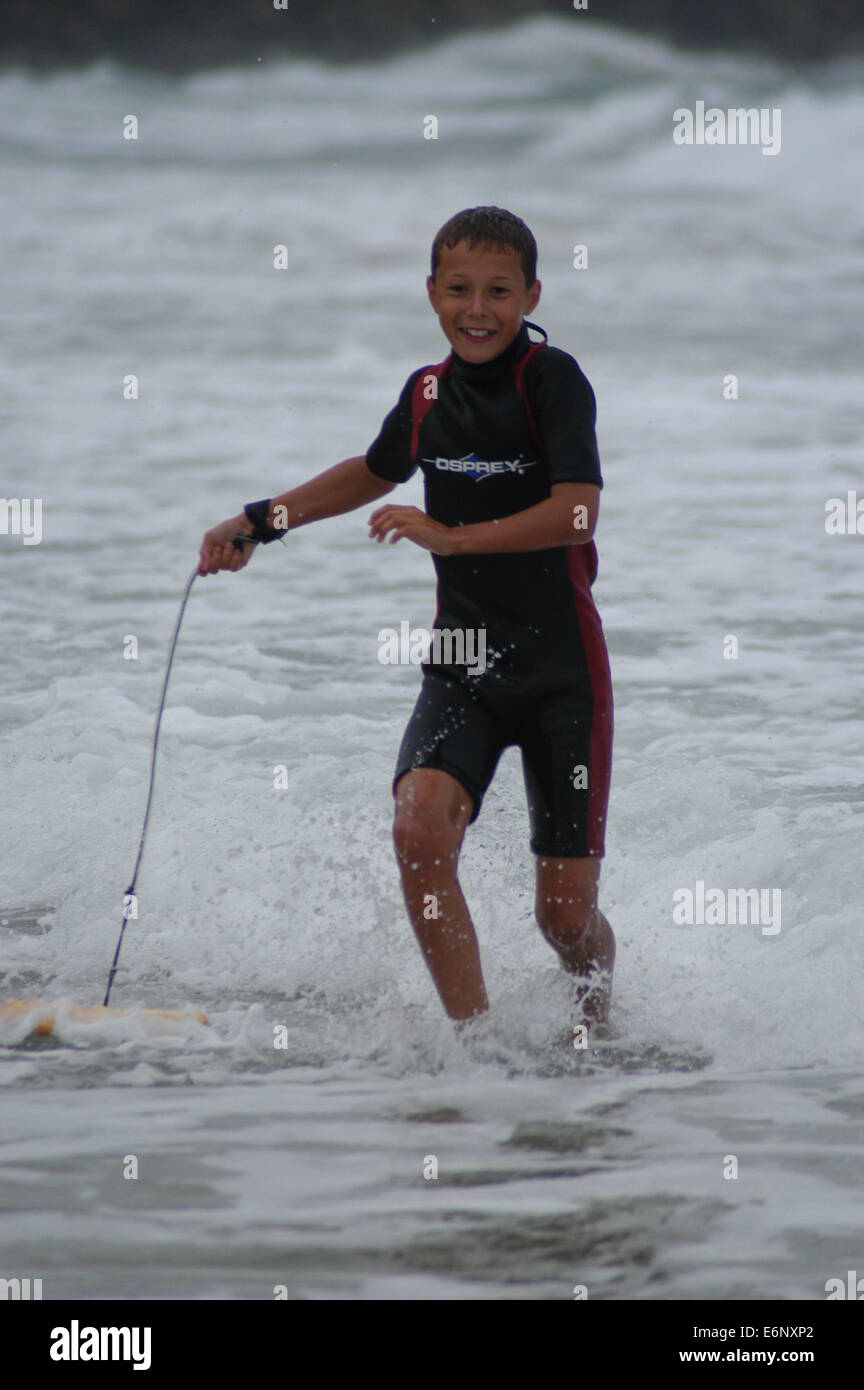 Junge männliche Jugendliche Surfen auf einem Bodyboard zu Fuß aus dem Meer ziehen seine Bodyboard im seichten Wasser mit weißen Spitzen hinter Stockfoto