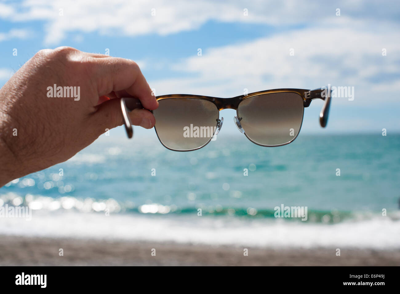 Hand, die Sonnenbrille mit Blick auf das Meer vom Strand entfernt Stockfoto