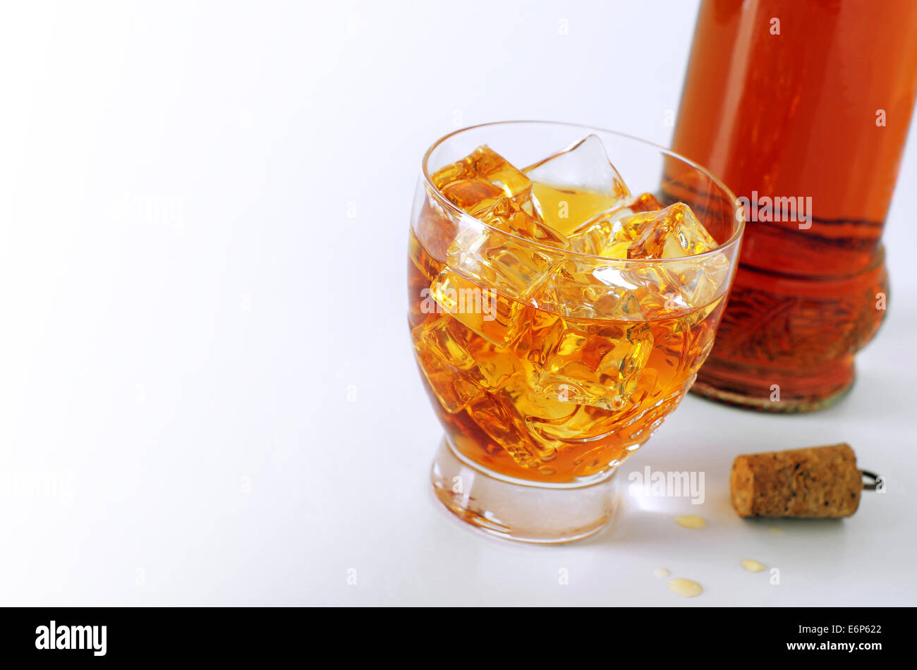 Alkoholisches Getränk in ein Glas mit Eiswürfeln und eine Flasche und Korken auf weißem Hintergrund Stockfoto