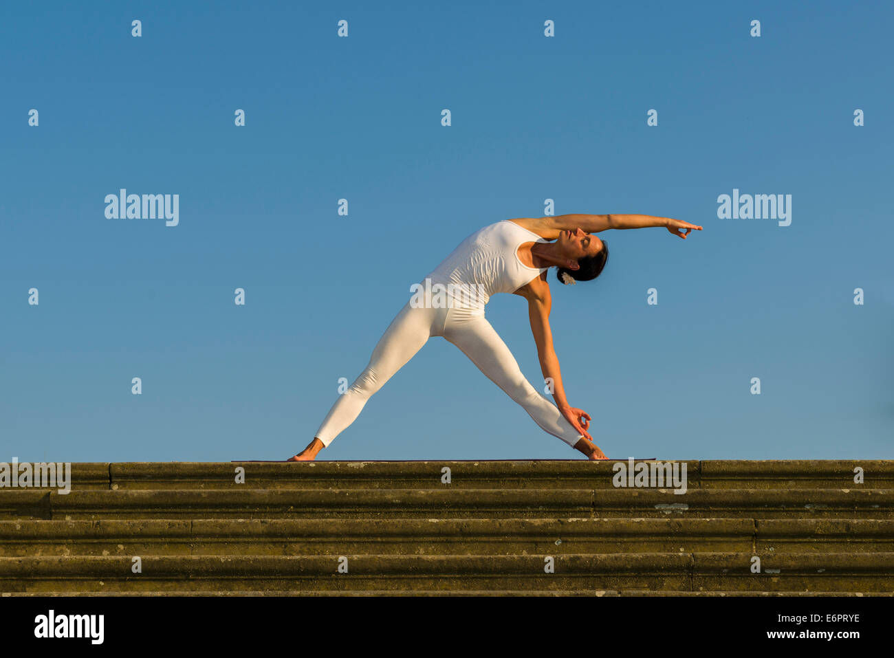 Junge Frau Hatha Yoga im Freien praktizieren, zeigt die Pose Trikonasana, Dreieck Stockfoto
