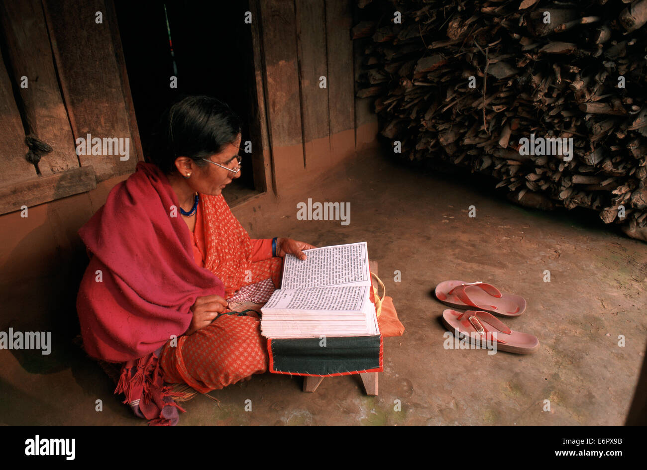Eine Frau liest ein hindu Buch in einem Ashram. Sie sitzt vor dem kleinen Haus wo sie bleibt (Nepal) Stockfoto