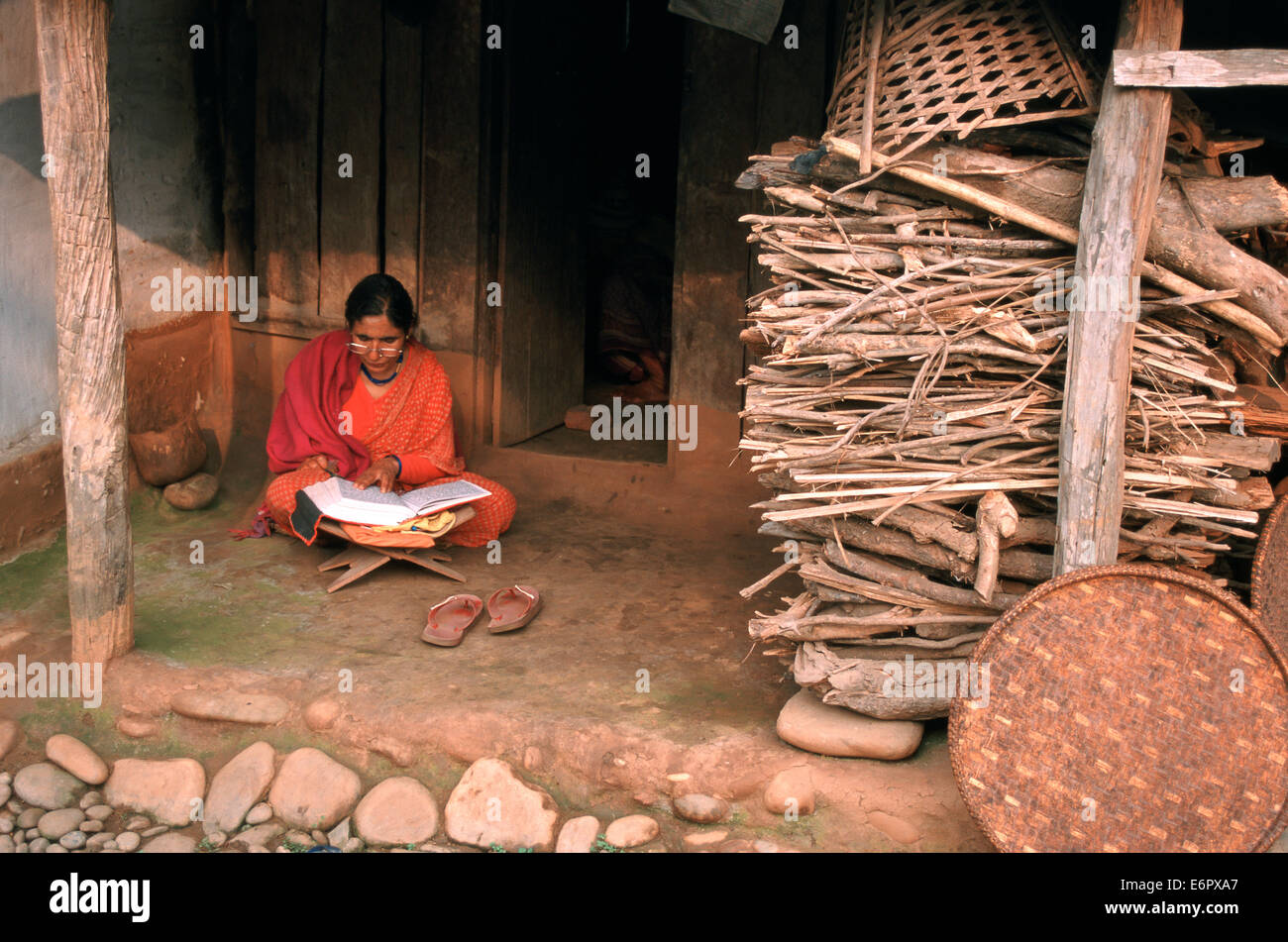 Eine Frau liest ein hindu Buch in einem Ashram. Sie sitzt vor dem kleinen Haus wo sie bleibt (Nepal) Stockfoto