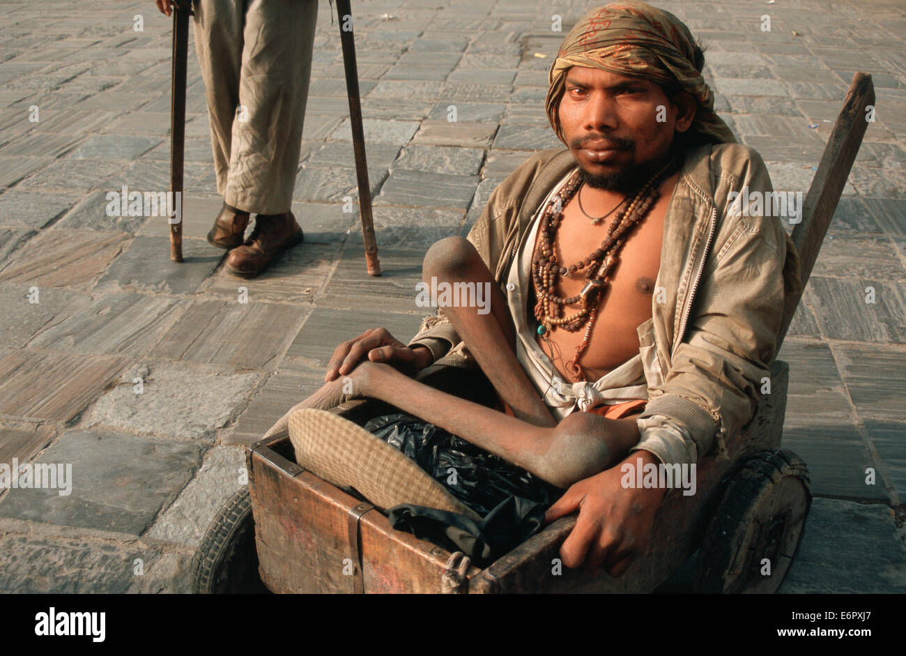 Bettler leiden Poliomyelitis auf einem Wagen. Im Hintergrund eine andere Bettler mit Krücken (Nepal) Stockfoto