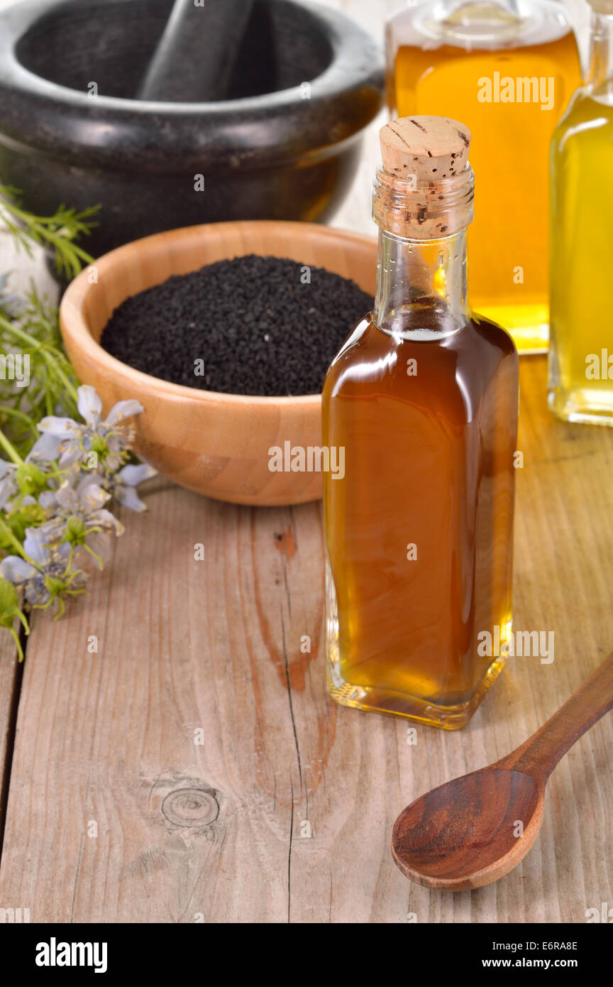 Nigella Sativa Öl in eine Flasche und Nigella Samen und Blumen auf hölzernen Hintergrund. Schwarzkümmel Heilung Kraut. Kalt gepresst. Stockfoto