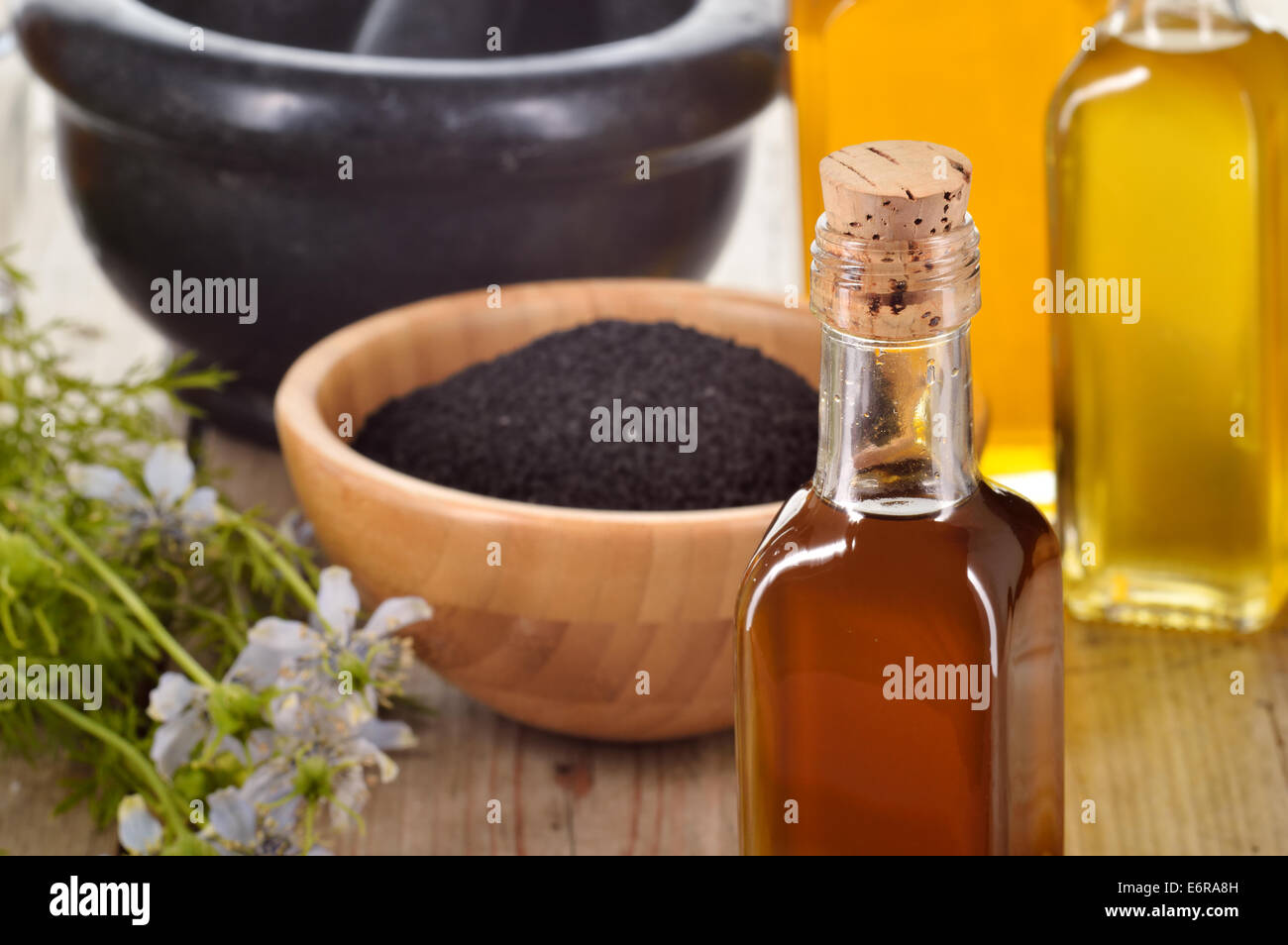 Nahaufnahme von Nigella Sativa Öl in eine Flasche gegen Nigella Samen und Blumen auf hölzernen Hintergrund. Schwarzkümmel Heilung Kraut. Stockfoto