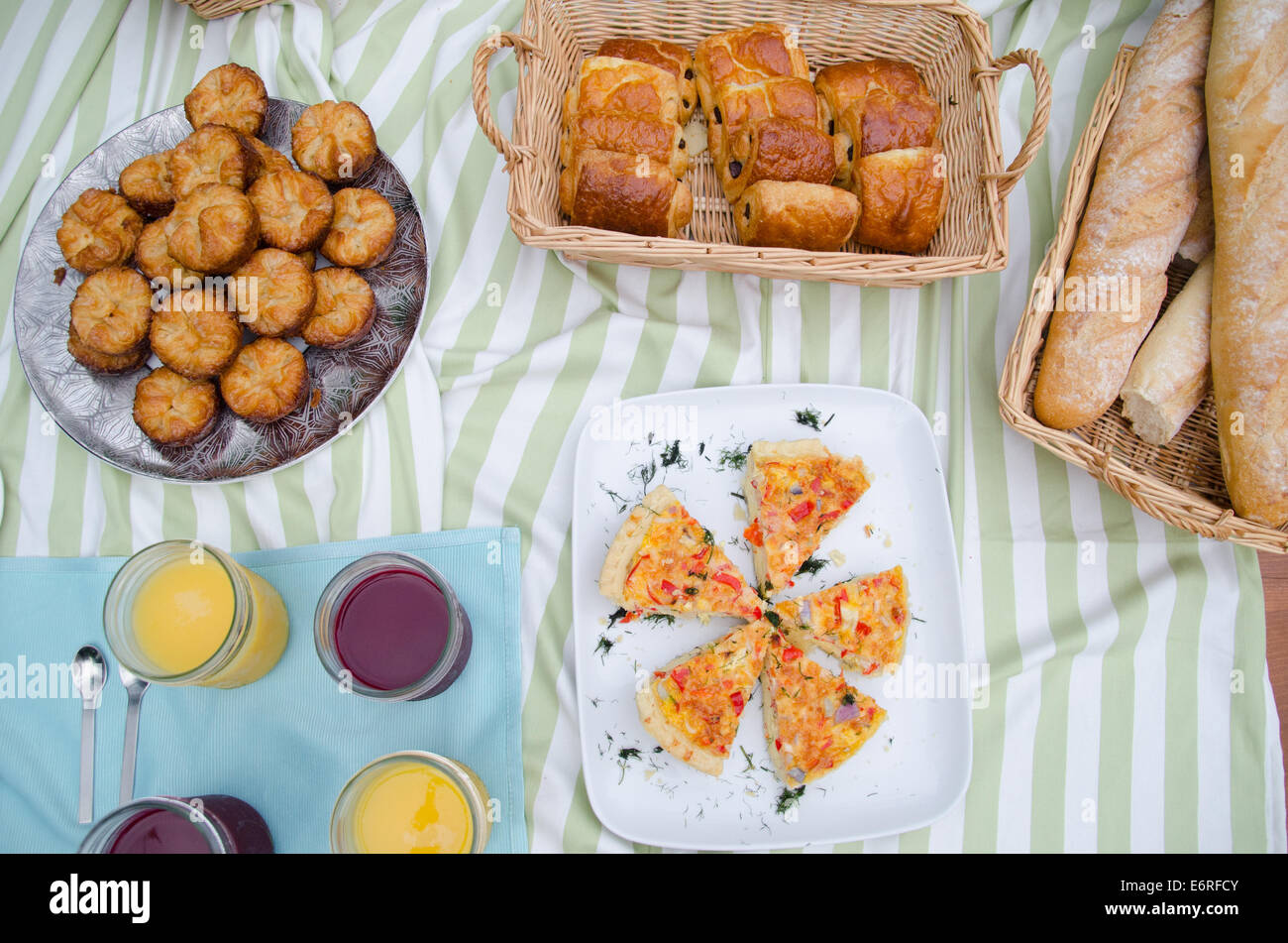 Picknick-Frühstück mit Saft, Gebäck, Croissants, Brotkorb, Tischdecken, Geschirr, Baguettes auf einem Tisch verteilen Stockfoto