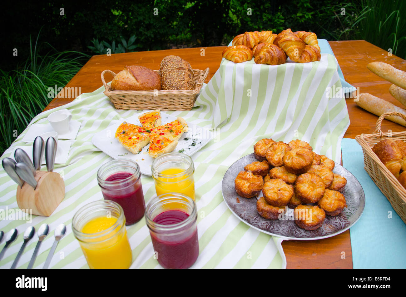 Picknick-Frühstück mit Saft, Gebäck, Croissants, Brotkorb, Tischdecken, Geschirr, Baguettes auf einem Tisch verteilen Stockfoto