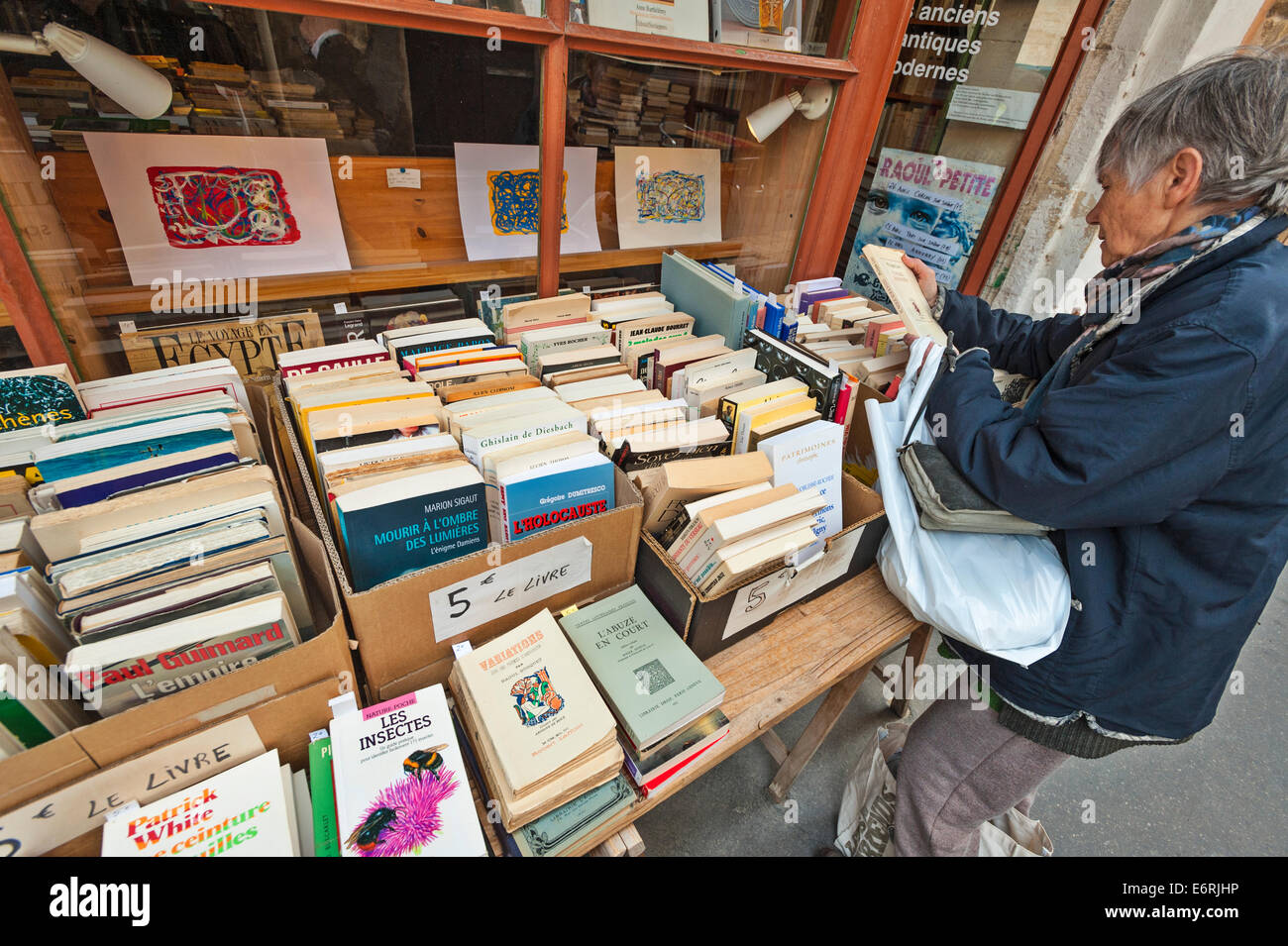 Eine Französin durchsuchen Boxen Bücher auf dem Display auf der Straße außerhalb eines Buchhändlers Shop in Roussillon, Frankreich Stockfoto