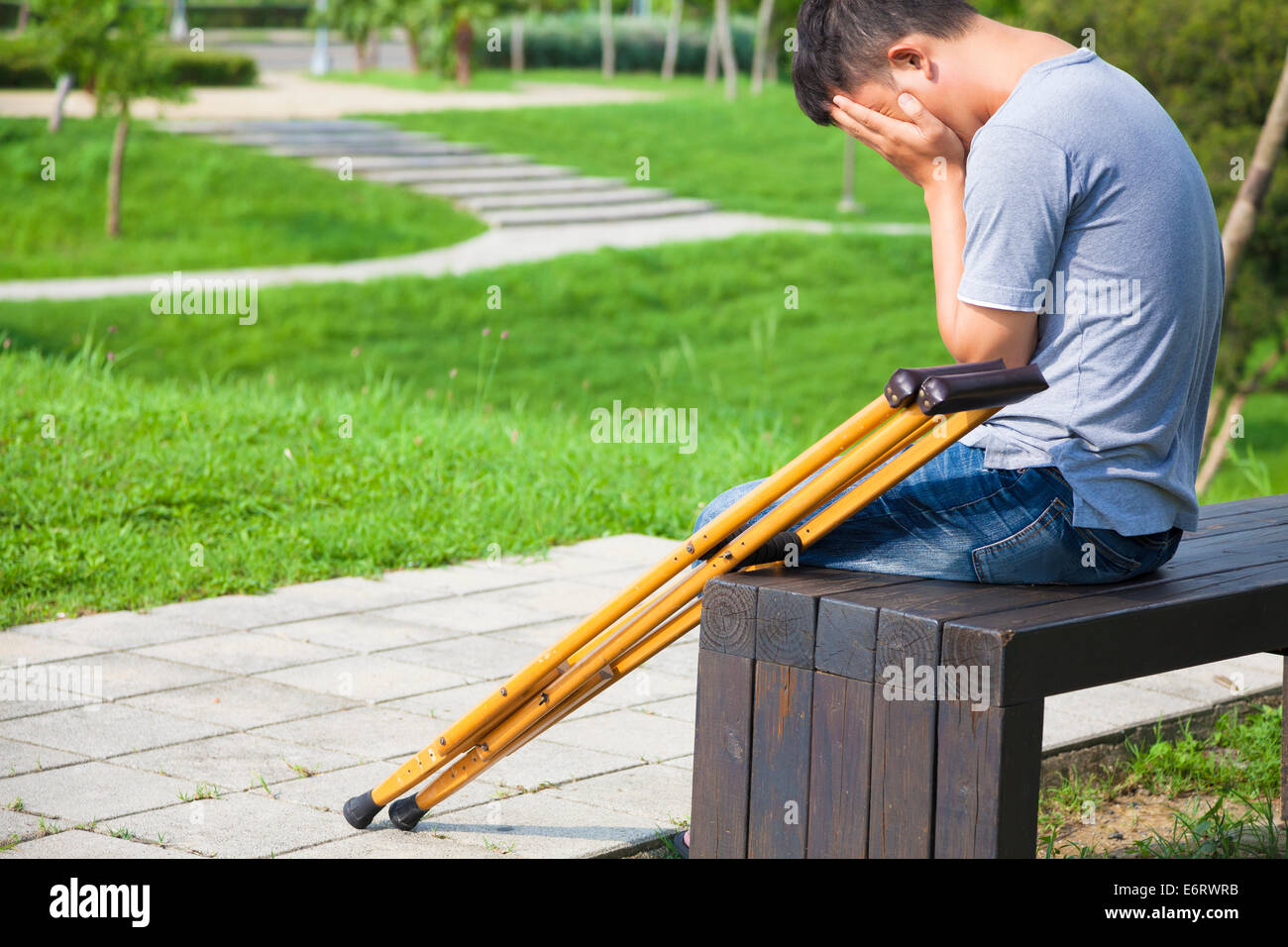 Verletzten Mann mit Krücken auf einer Bank sitzend Stockfoto