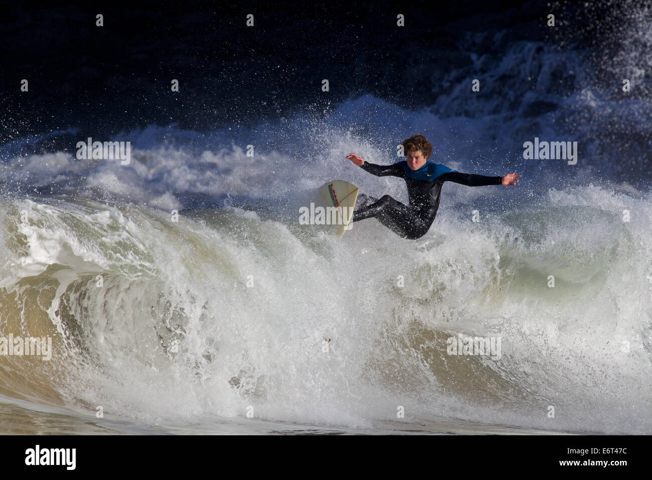 Eine Surfer schwebt über der Oberseite einer brechenden Welle, hervorgehoben durch die Sonne vor dem Hintergrund der Klippen Stockfoto