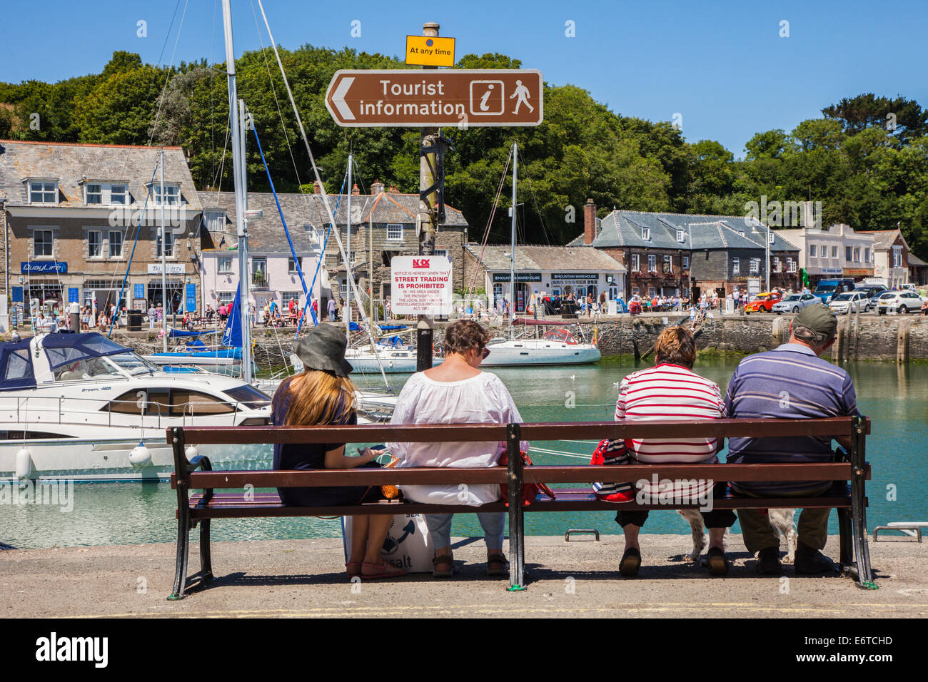 Touristen sitzen auf einer Bank mit Blick auf den Hafen in Padstow, Cornwall, England, UK Stockfoto