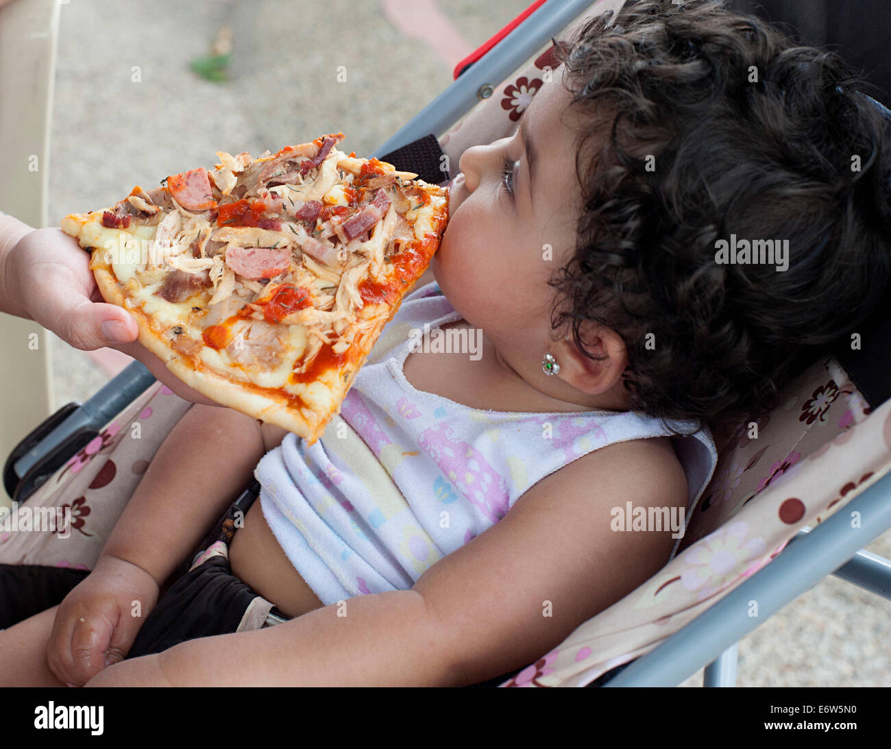 Lady ernährt Stück Pizza auf einjährige Mädchen im Kinderwagen. Bogota Kolumbien. Stockfoto