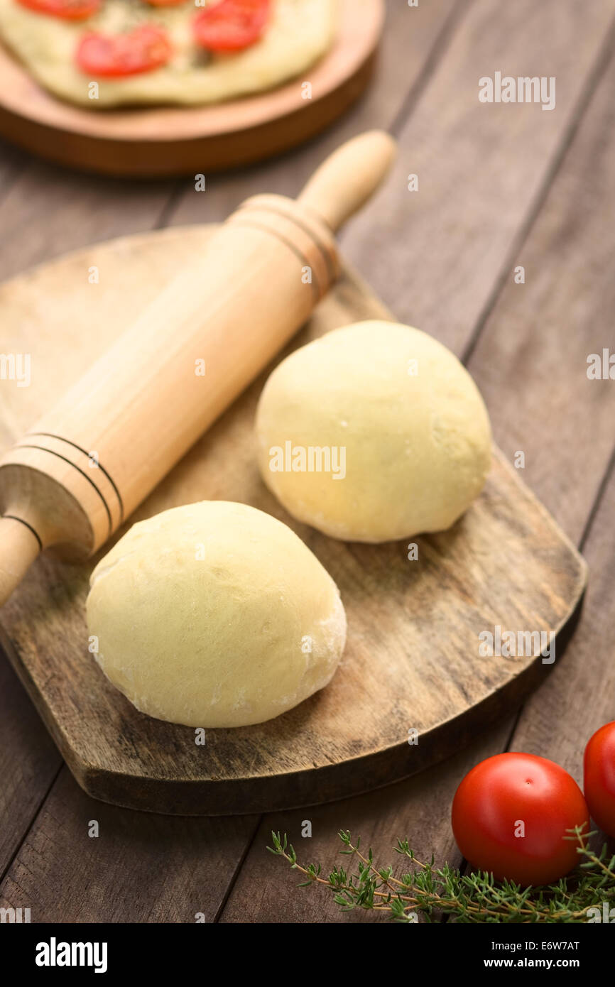 Kleine Kugeln aus Hefeteig für Pizza oder Fladenbrot mit Nudelholz auf Holzbrett, Tomaten und Thymian in der front Stockfoto