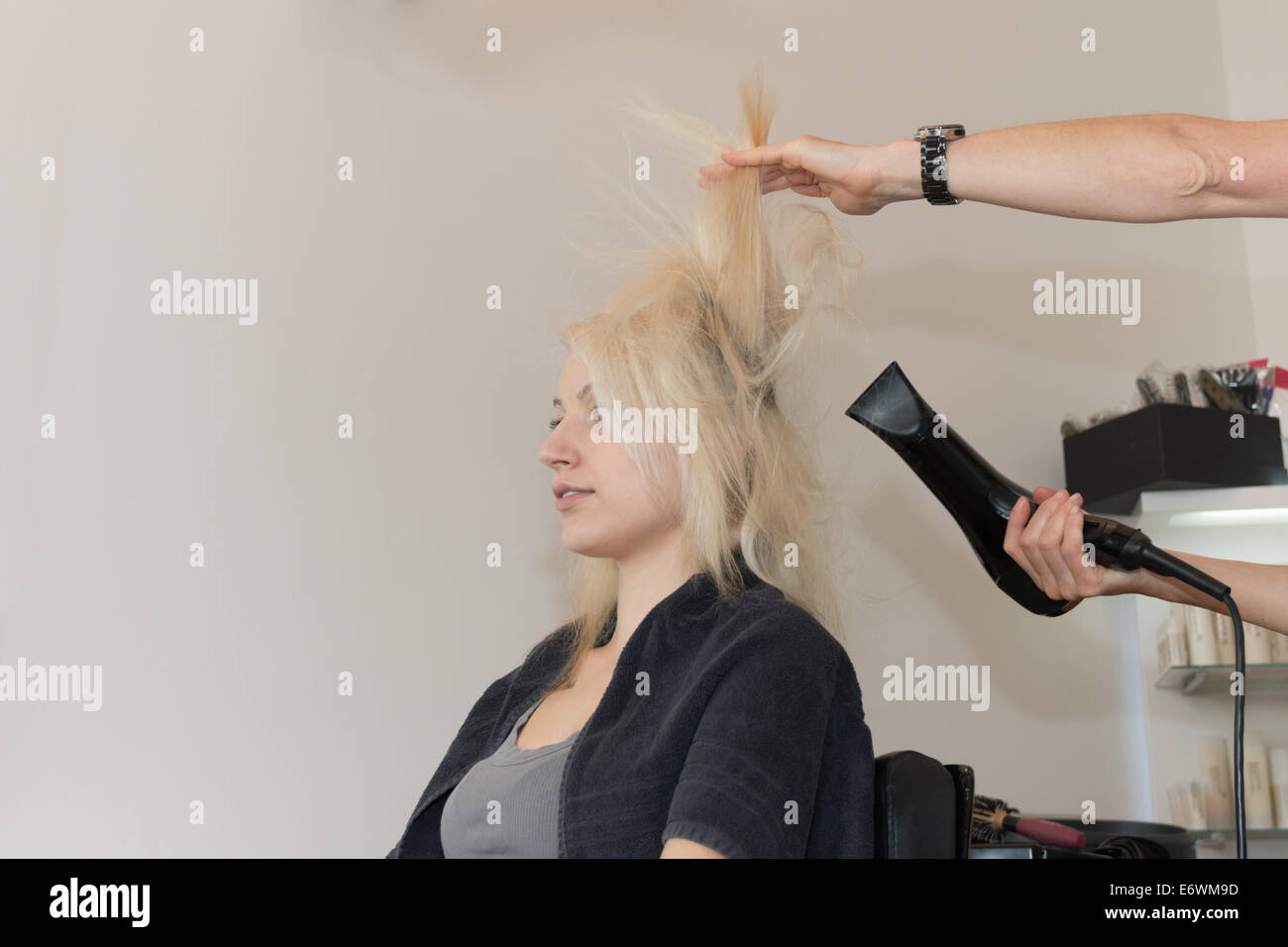 Schöne blonde Mädchen sitzen, ich Haare getrocknet. Hände von Friseur sichtbar, mit Fön Stockfoto