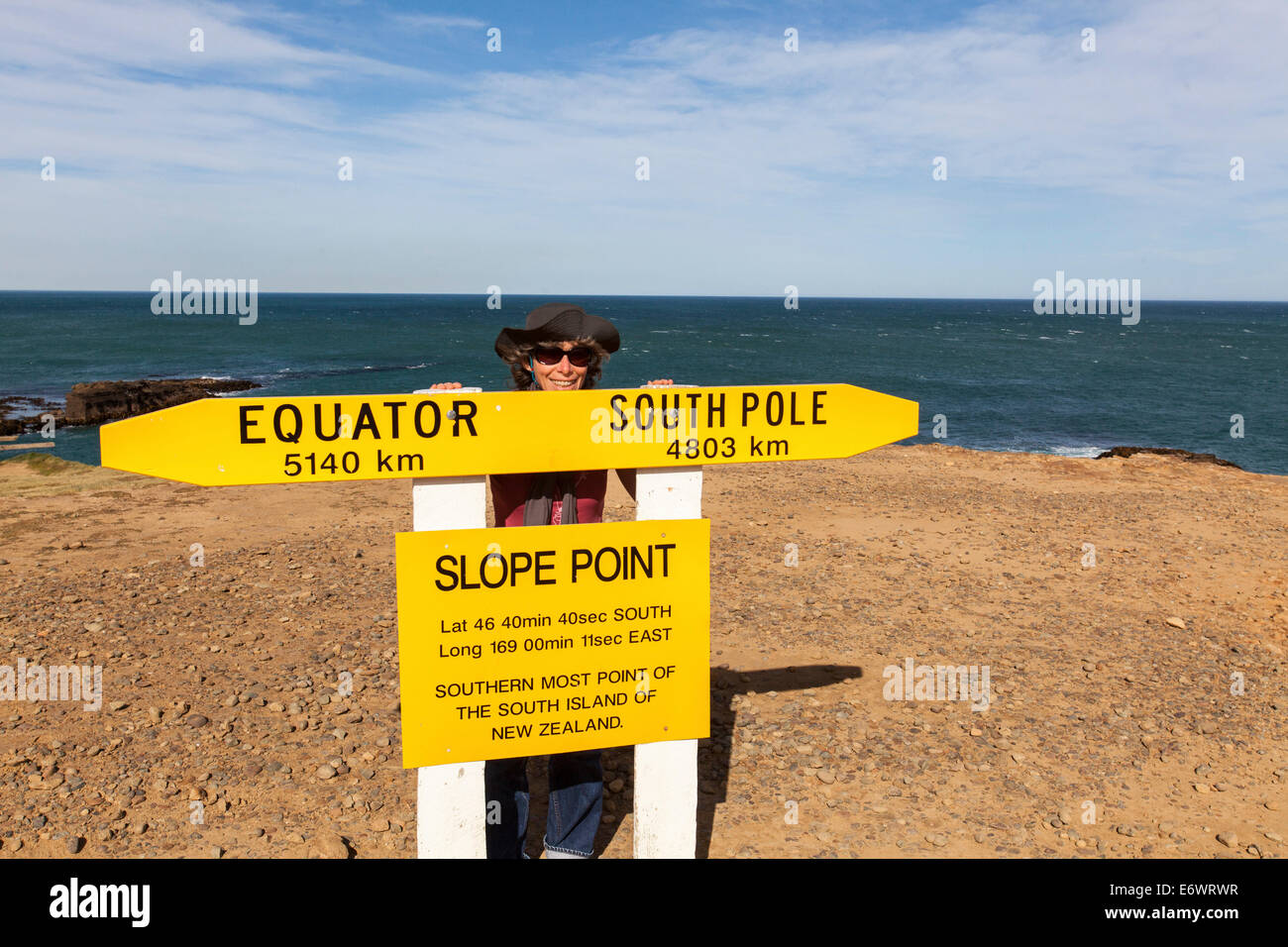 Frau hinter einem Schild mit der südlichste Punkt der Südinsel, Slope Point, Catlins, Südinsel, Neuseeland Stockfoto