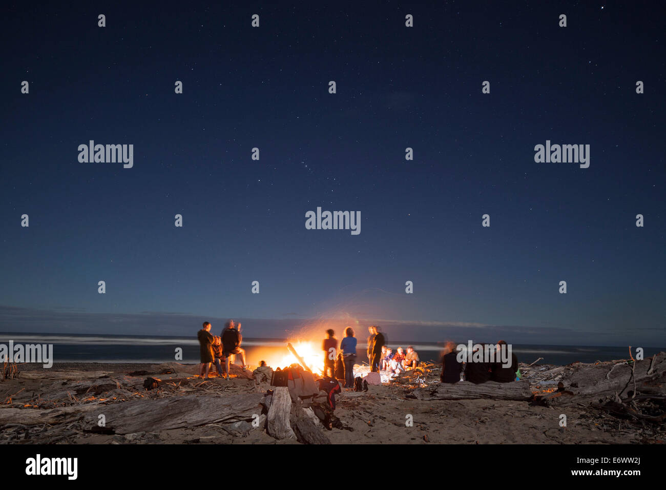 Lagerfeuer mit Treibholz am Strand, Gruppe von Menschen rund um ein Lagerfeuer, West Coast, Südinsel, Neuseeland Stockfoto