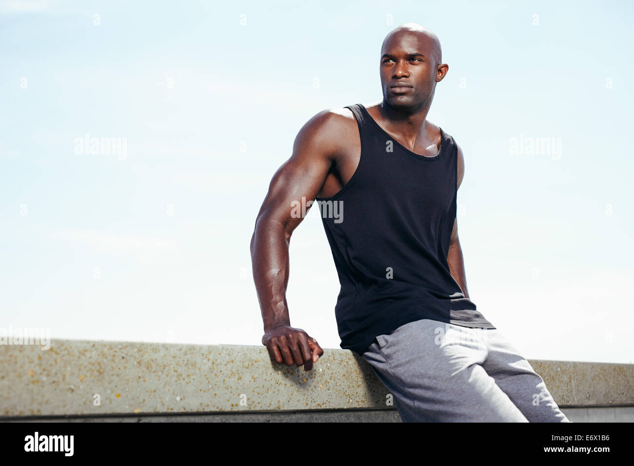 Bild der muskulösen jungen Mann gegen Himmel wegsehen bei Exemplar im Freien sitzen. Fit-afrikanische männlichen Modell. Stockfoto