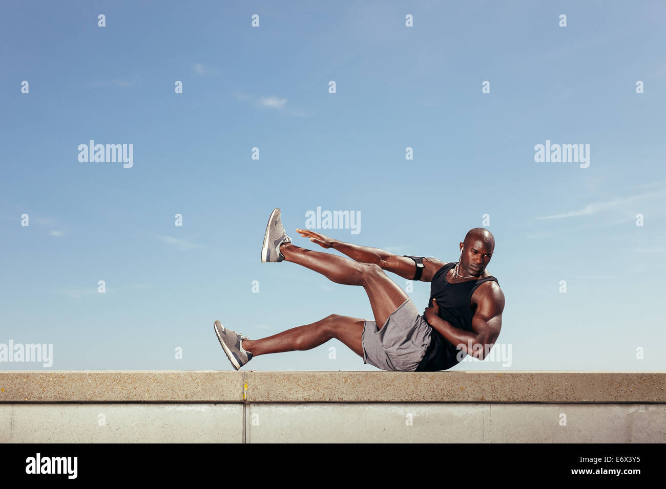 Passen Sie jungen Mann stretching Training im Freien zu tun. Muskulösen jungen Fitness-Modell Ausübung gegen Himmel. Stockfoto