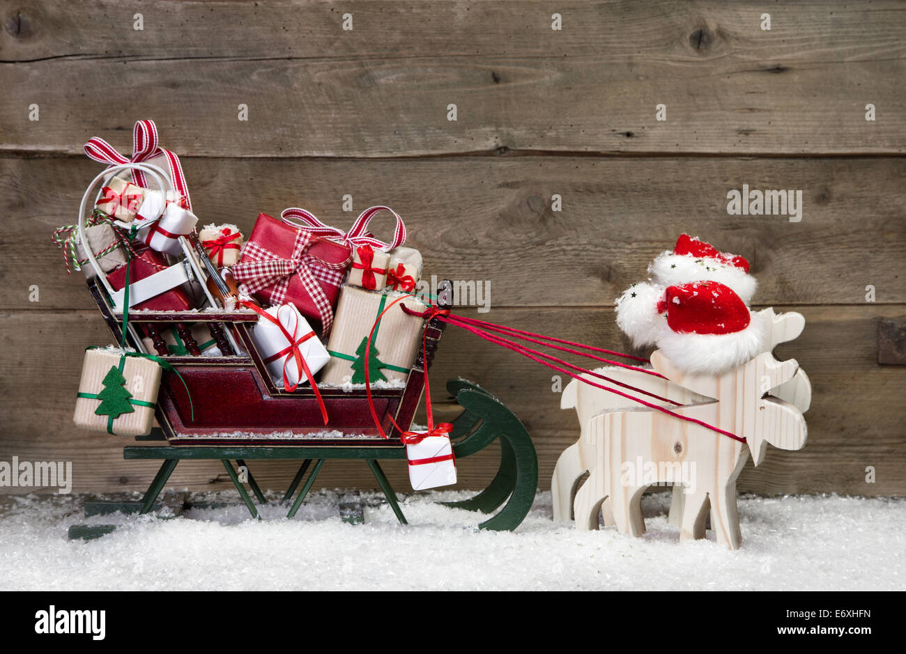 Weihnachtskarte-Dekoration: Elche Santa ziehen Schlitten mit Geschenken auf einem hölzernen Hintergrund - lustige Grußkarte im Landhausstil Stockfoto