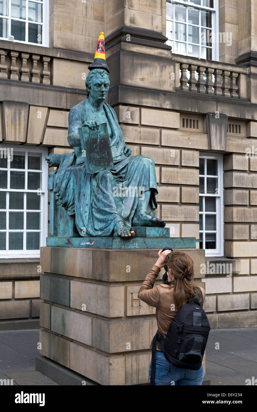 Eine junge Frau fotografiert die Statue des David Hume mit "No Parking" Kegel auf dem Kopf auf der Royal Mile in Edinburgh, Schottland, UK Stockfoto