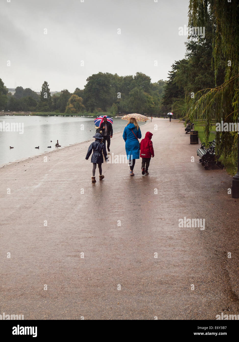 Menschen in Regenkleidung tragen Regenschirme zu Fuß neben dem serpentine Bootfahren See Hyde Park bei starkem Regen Stockfoto